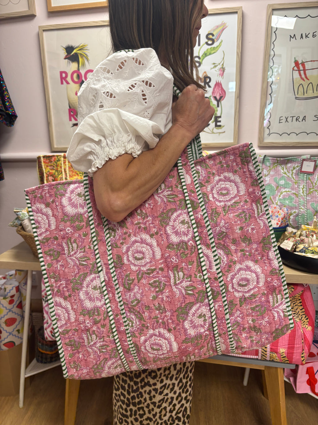 Person holding a pink floral tote bag in a store setting with artwork on the wall.