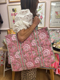 Person holding a pink floral tote bag in a store setting with artwork on the wall.