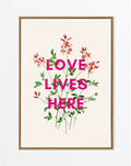 A framed art print with a vintage floral design and the text 'LOVE LIVES HERE' in bold letters.