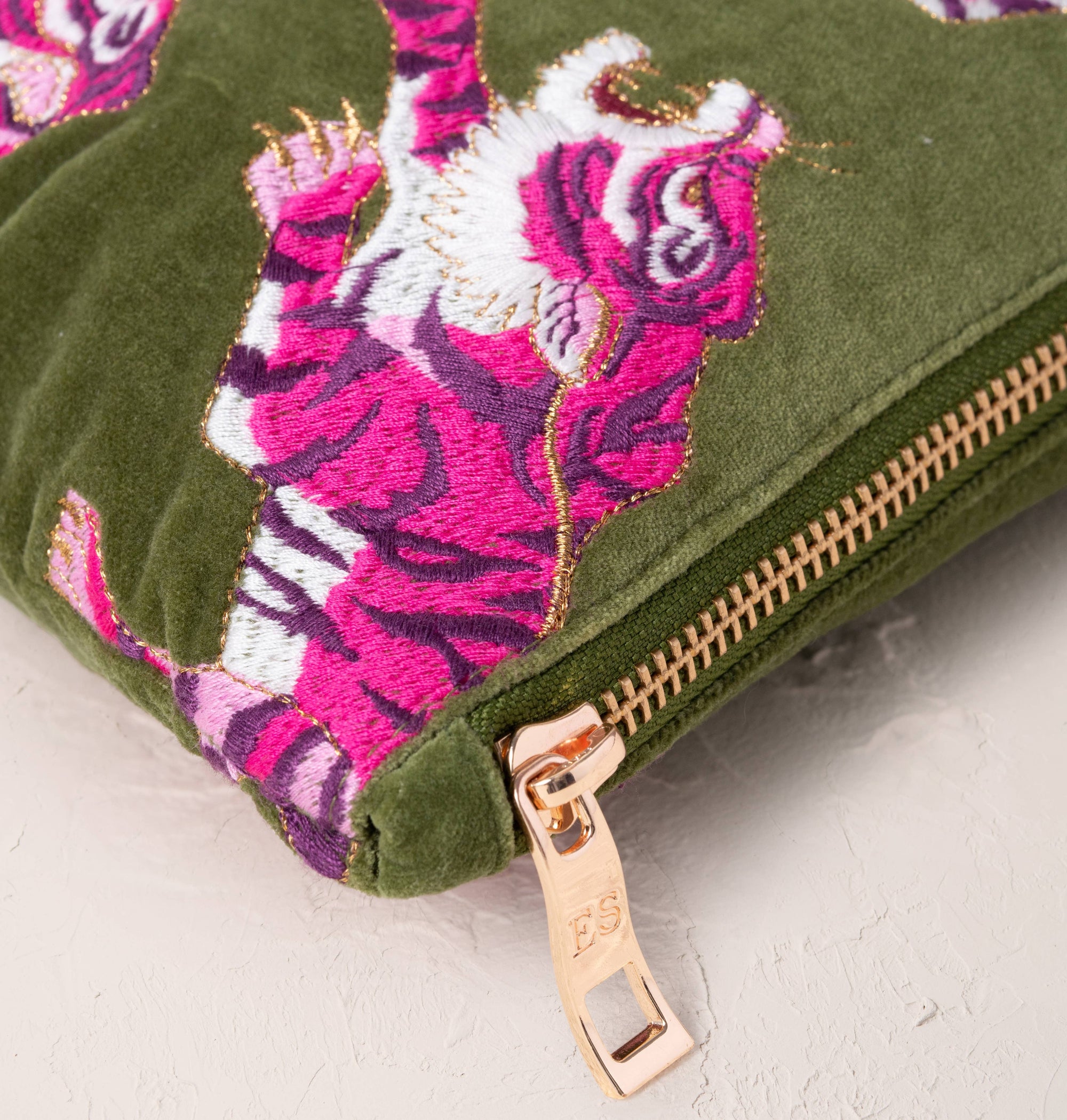 Green clutch with pink tiger design and gold zipper on a light gray background