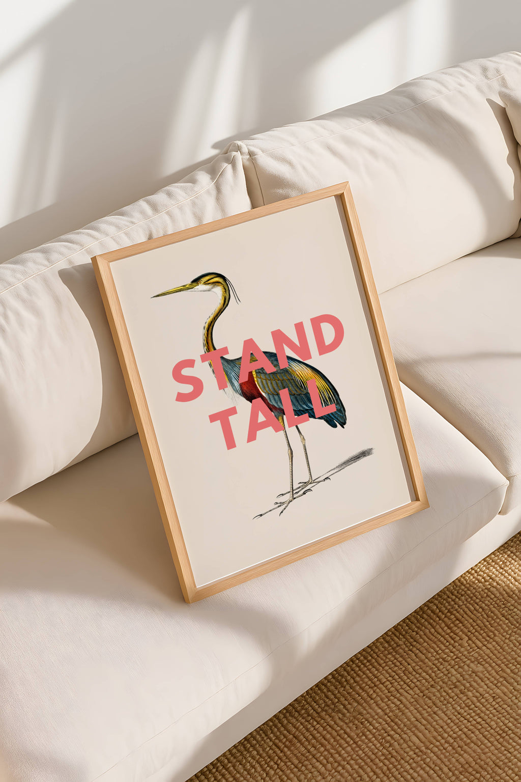 Framed artwork with a colorful bird illustration and 'Stand Tall' text on a beige sofa.