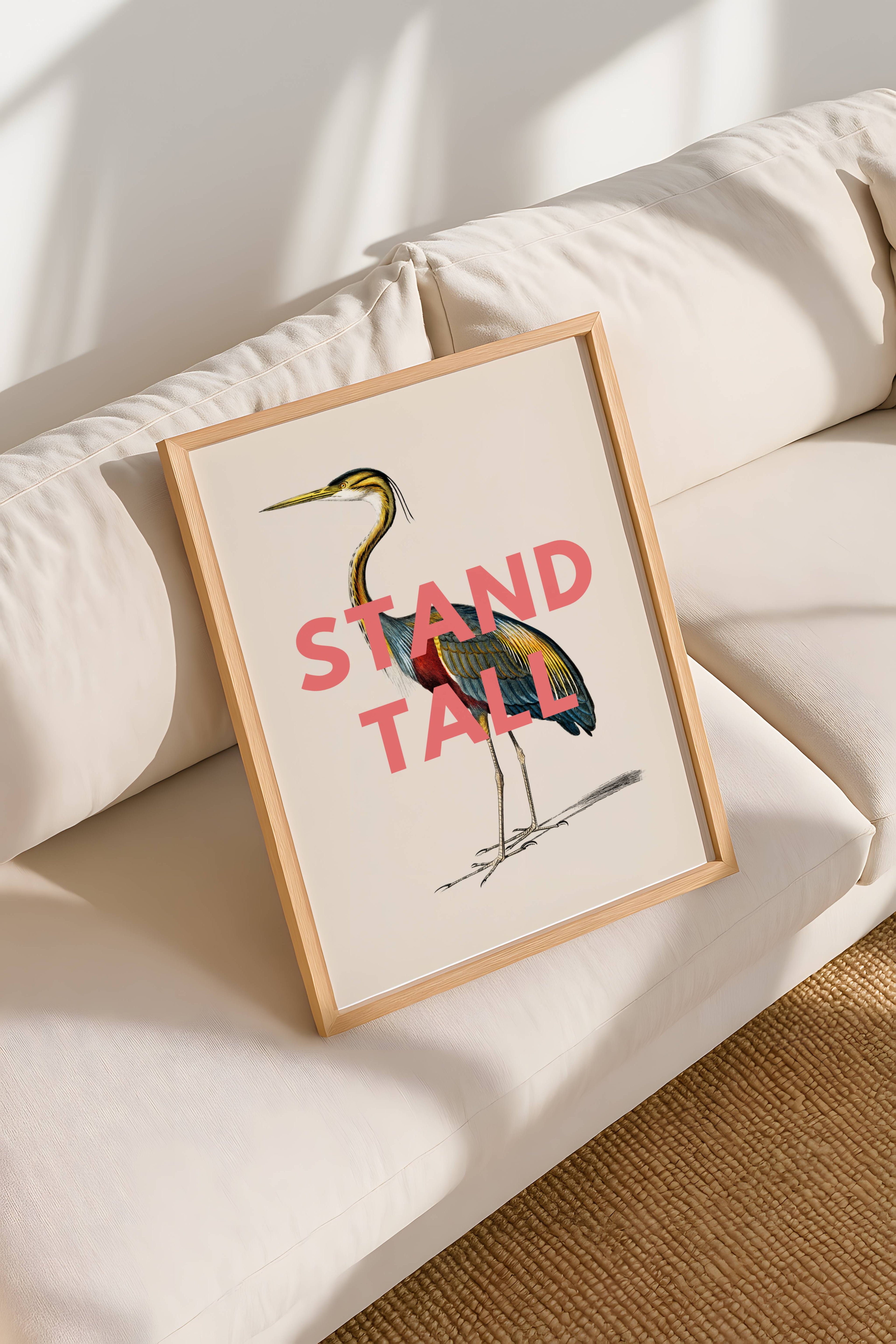 Framed artwork with a colorful bird illustration and 'Stand Tall' text on a beige sofa.