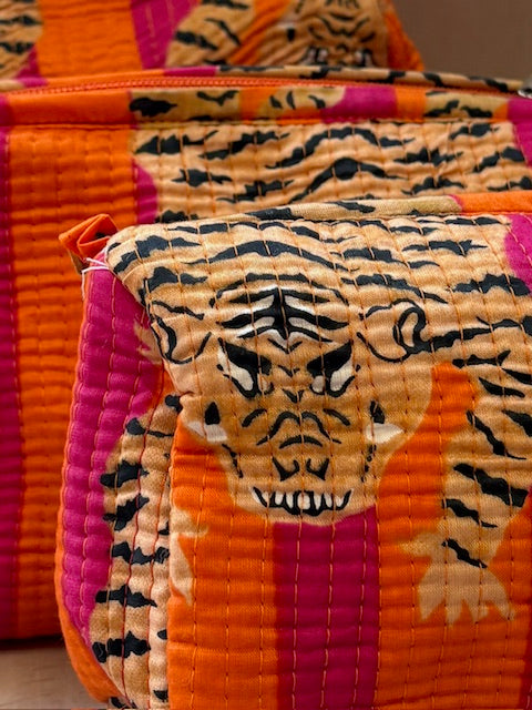 A close-up of a quilted fabric pouch featuring a tiger face print in orange, pink, beige, and black, with a matching zippered case in the background.