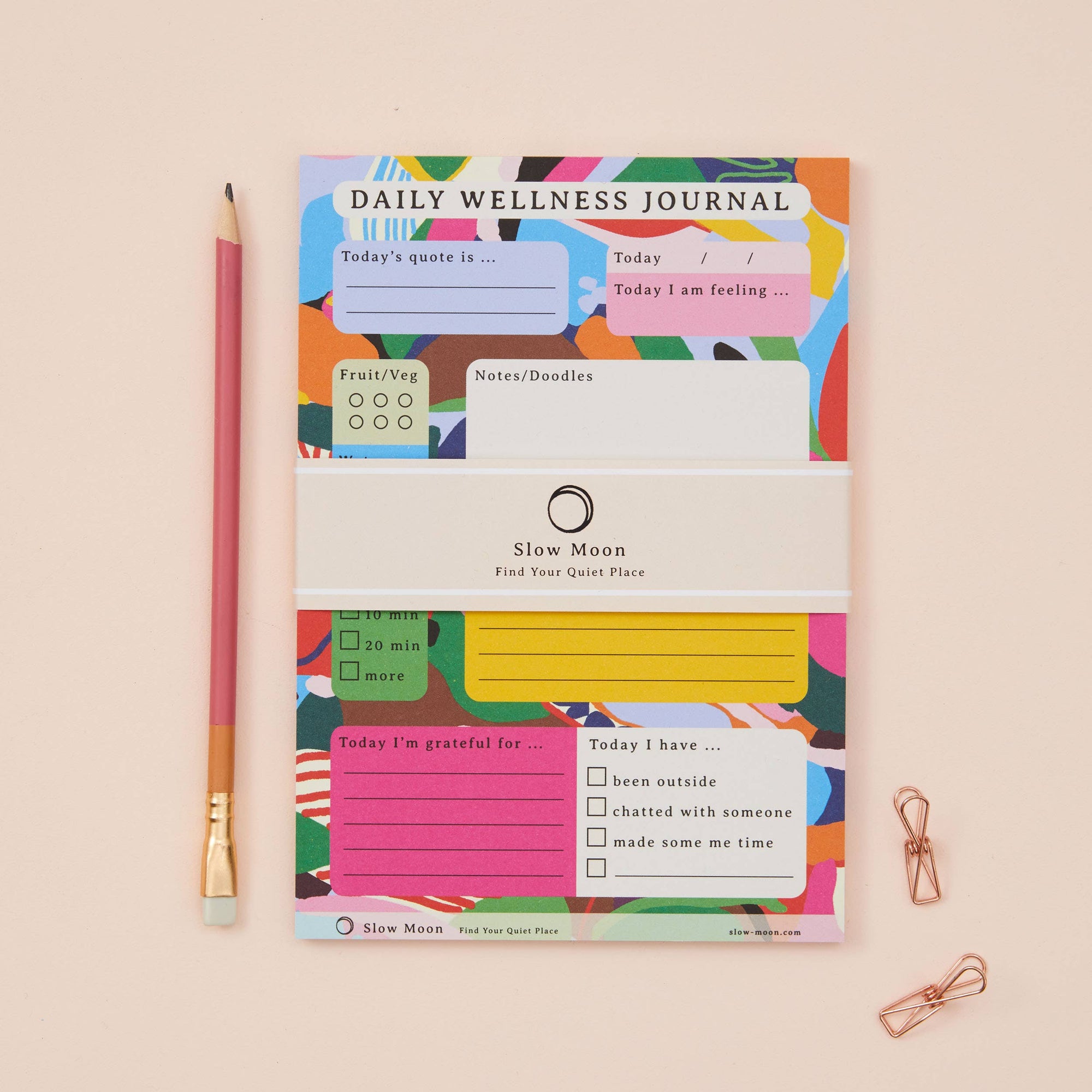 Colorful daily wellness journal with a pencil and paper clips on a beige background